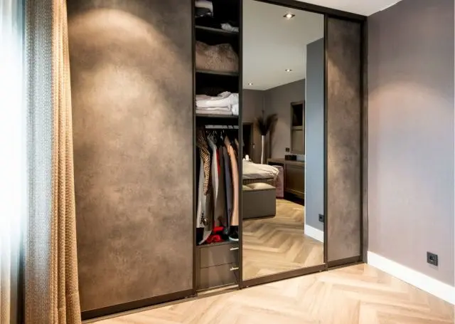 Schuifdeurkast met spiegel en open garderobevak in een slaapkamer
