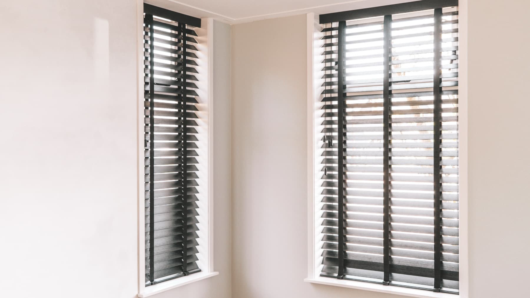 Twee donker houten jaloezieën in een hoek van een lichte kamer