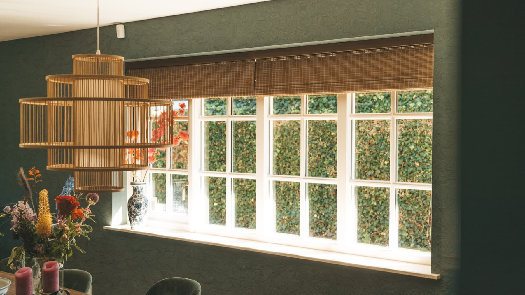 Woodweave-rolgordijnen boven brede ramen in een eetkamer met groene muren